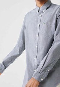 Sininen ja valkoinen ruudullinen nappipaita, jossa pitkät hihat, kaulus ja rintatasku. Paidassa on valkoiset napit ja rintamuksessa logo.