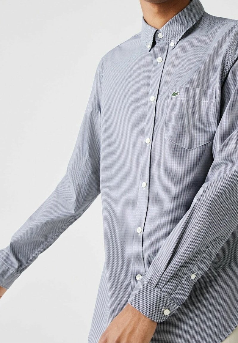 Sininen ja valkoinen ruudullinen nappipaita, jossa pitkät hihat, kaulus ja rintatasku. Paidassa on valkoiset napit ja rintamuksessa logo.