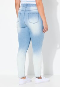 Jeggings de mezclilla descoloridos en azul claro con cintura elástica, bolsillos traseros y piernas ajustadas, combinados con zapatillas blancas.