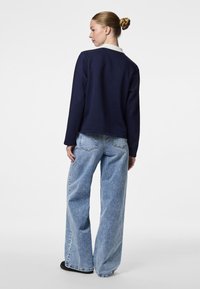 Marineblå sweatshirt med kontrastfarget hvit krage, kombinert med lyseblå vide bukser som har en avslappet passform og myk tekstur.