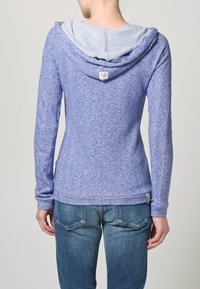 Lila huva-tröja med en texturerad yta, med en ljusblå innerhuva. Figursydd design med långa ärmar och en nedre fåll.