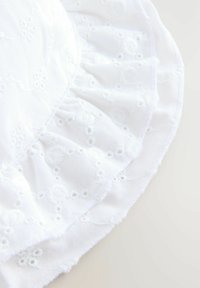 Tessuto di cotone bianco ricamato con bordo arricciato, caratterizzato da motivi floreali e piccoli dettagli ad occhio di bue, creando un aspetto testurizzato.