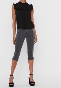 Haut sans manches noir avec un col volanté, associé à un jean gris court et des sandales à talons hauts noires. Texture de tissu lisse.