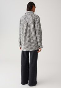 Grau-weiße gemusterte oversized Hemdjacke mit Kragen und langen Ärmeln, kombiniert mit dunklen, weiten Jeans. Weiche Textur.