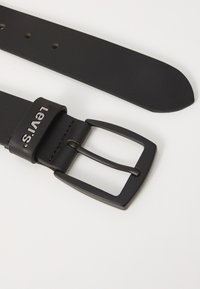 Black leather belt with a matte black metal buckle. Features a subtle embossed logo and multiple adjustment holes along the strap.