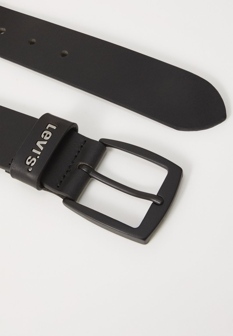 Ceinture en cuir noir avec une boucle en métal noir mat. Présente un logo légèrement embossé et plusieurs trous d'ajustement le long de la sangle.