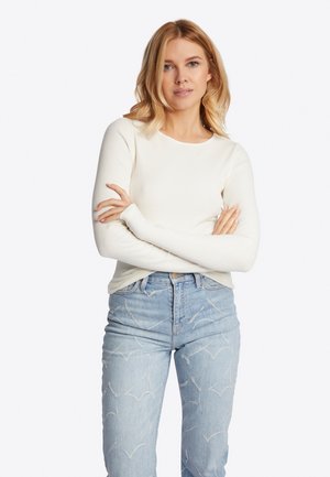 Long-sleeve ribbed top in white, featuring a round neckline, paired with light blue jeans showcasing a subtle bird-patterned design.