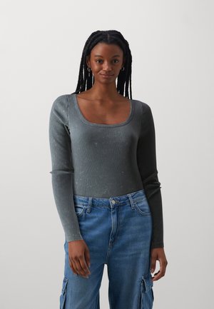 Langärmliger, dunkelgrauer gerippter Body mit quadratischem Ausschnitt, kombiniert mit hellblauen Jeans aus Denim mit Cargo-Taschen.