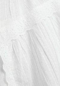 Robe en tissu blanc avec des plis texturés et une bordure brodée festonnée comportant de petits détails en œillet. Design lisse, léger et aérien.