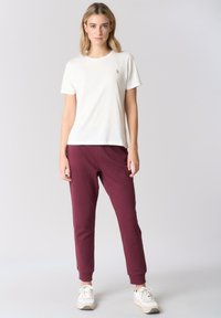 T-shirt bianca in cotone con maniche corte e piccolo logo, abbinata a pantaloni jogger bordeaux con orli a coste. Sneakers completano il look.