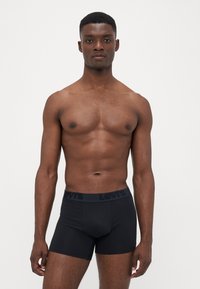 Boxers pretos com uma faixa elástica de marca, feitos de um material suave e elástico. O design apresenta uma forma ajustada e pernas de comprimento médio.