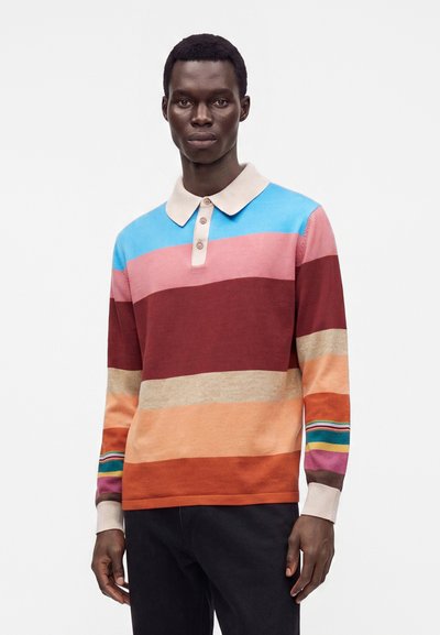 Homme portant un polo à manches longues avec de larges rayures horizontales bleu, rose, bordeaux, beige, orange et multicolores sur la manche.