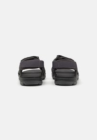 Sorte sandaler med justerbar stroppdesign, som har gummisåler og teksturerte stoffstropper. Minimalistisk, åpen bakstil som passer til uformelt bruk.