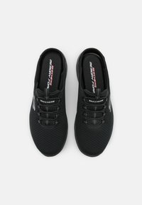 Baskets de sport noires avec une tige en maille, des lacets élastiques et une semelle intérieure en mousse à mémoire de forme. Présente le logo "Skechers" sur les côtés et les semelles intérieures.