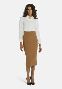 Jupe crayon marron avec une taille haute et une texture lisse, associée à une chemise blanche à boutons. Des escarpins noirs à talons hauts complètent le look.