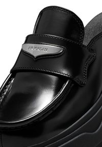 Sanda negra de cuero deslizante con acabado brillante, correa acolchada con la marca en plata "AIR JORDAN", plantilla texturizada y suela gruesa.