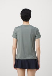 Pelēks īso piedurkņu sporta krekls ar gludu tekstūru, ar apaļu izgriezumu un pieguļošu dizainu, kopā ar tumši zilu svārku ar platu apakšu.