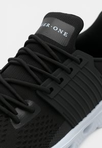 Μαύρο αθλητικό παπούτσι με υφασμένο άνω μέρος, επίπεδα κορδόνια και λαστιχένια σόλα. Διαθέτει λεία ετικέτα και καλουπωμένες λεπτομέρειες στα πλευρά.