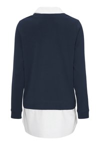 Mörkblå långärmad topp med en vit skjorta under. Mjuk tyg, rund nederkant och ribbade ärmslut. Enkelt, lager-på-lager design.