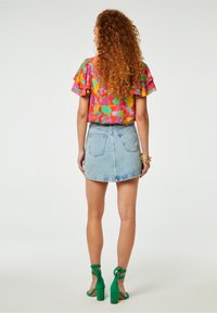 Růžový vršek s květinovým vzorem a volánkovými rukávy, doplněný světlou modrou džínovou sukní a zelenými sandály na vysokém podpatku s pásky.