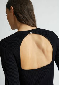 Top nero a coste con una grande schiena scoperta, fissato da un piccolo dettaglio metallico. La consistenza morbida e il design aderente esaltano la forma.