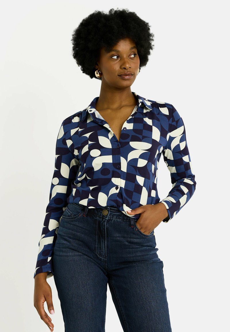 Chemise à boutons bleu marine, ornée de motifs géométriques blancs et bleu clair. Manches longues avec col et poignets, tissu lisse.