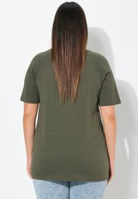 Camiseta de manga corta verde oliva con un ajuste relajado, escote redondeado y mangas en raglán. Confeccionada en una tela suave con una textura lisa.