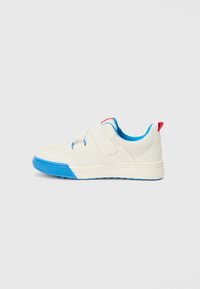 White sneakers with a textured upper, blue accents on the sole and lining, and a red tab at the heel; features a hook-and-loop strap.