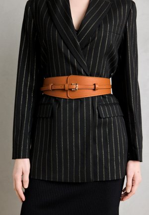 Black pinstripe blazer with gold accents, featuring a brown leather belt, two front pockets, and a tailored fit. Ribbed black skirt below.