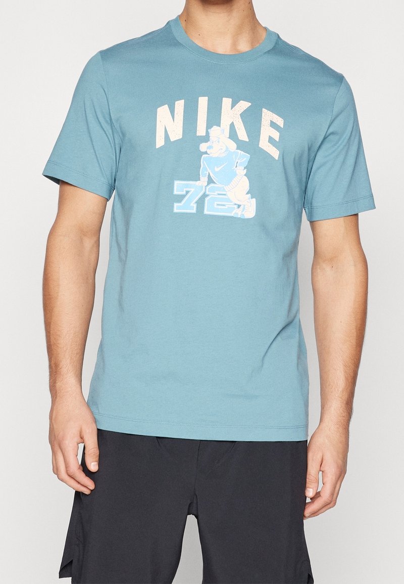 Homme portant un t-shirt bleu Nike avec un chien de dessin animé et le numéro 78 imprimé sur le devant, associé à un short noir.