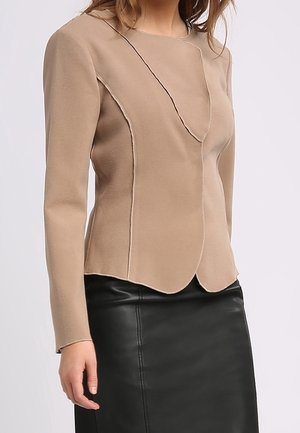 Haut beige à manches longues avec un ourlet festonné et des surpiqûres contrastantes, confectionné dans une texture douce, associé à une jupe en cuir noire.