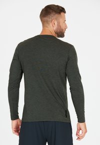 Pitkähihaisessa t-paidassa on tummanvihreä väri, se on valmistettu teksturoidusta kankaasta, siinä on pyöreä kaula-aukko ja hienovarainen kuosi selässä.