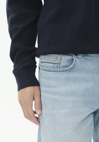 Tamsiai mėlynas tekstūruotas megztinis su ilgomis rankovėmis derinamas su šviesiai mėlynomis džinsinėmis kelnėmis, turinčiomis subtilų šviesinimą ir klasiką penkių kišenių dizainą.