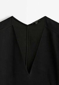 Schwarzes Kleidungsstück mit tiefem V-Ausschnitt und strukturierten Schultern, aus glattem Stoff mit verdecktem Reißverschluss im Rücken und minimalen Nähten.