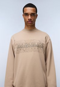 Felpa beige con scollatura rotonda e maniche lunghe, caratterizzata da una stampa grafica screpolata di "Napapijri" in marrone sul davanti.