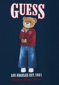 Το γραφικό δείχνει έναν χαρακτήρα αρκούδας που φοράει κόκκινο πουλόβερ με λευκές ρίγες και καρδιά, μπλε τζιν και λευκά παπούτσια πάνω σε σκούρο μπλε φόντο.