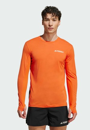 Langärmliges, leuchtend oranges Sportshirt mit strukturierten Seitenpaneelen. Verfügt über einen runden Ausschnitt und ein weißes "TERREX"-Logo auf der Brust.