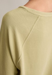Jasnozielony bawełniany sweter o fakturowanym, prążkowanym splocie. Posiada lekko zakrzywiony dekolt oraz widoczne detale szwów na ramionach.