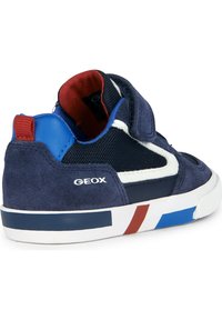 Zapatillas de ante azul marino con paneles de malla, acentos blancos, tab de talón azul y rayas de colores en la suela. Cierre de velcro para un uso fácil.