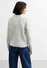 Grijze gebreide trui met een getextureerd ruitpatroon op de mouwen, ribgebreide zoom en een losse pasvorm, gecombineerd met donkerblauwe wijde jeans.