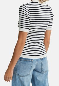 Dziergany top z krótkim rękawem w niebiesko-białe poziome paski, z prążkowaną teksturą i białym kołnierzykiem. Zestawiony z jasnoniebieskimi dżinsami.