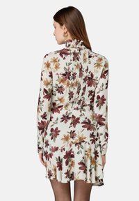 Langärmliges Blumenkleid in Weiß mit burgunderroten, gelben und grünen Mustern, das mit einem Rüschen-Ausschnitt und einem gesmockten Rückendetail versehen ist.