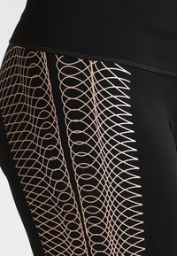 Leggings neri con un motivo geometrico testurizzato in rosa oro sul lato esterno, con una finitura in tessuto liscia e un design aderente.