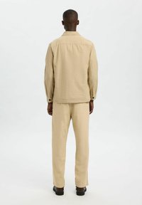Set di giacca e pantaloni in lino beige visto da dietro, caratterizzato da un taglio rilassato, maniche lunghe e design minimalista.