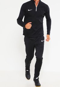 Tuta atletica nera realizzata in materiale leggero, con una parte superiore a zip a quarto e accenti con logo. I pantaloni hanno una vita elasticizzata.
