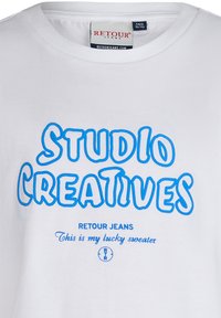 Biała bawełniana koszulka z niebieskim, wyraźnym napisem "STUDIO CREATIVES," a także "RETLOUR JEANS" i "To jest mój szczęśliwy sweter."