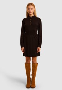 Czarna sukienka na długi rękaw z okrągłym kołnierzem, ozdobiona złotymi guzikami i taliowana. Dopasowana do niej jasnobrązowe zamszowe kozaki za kolano.