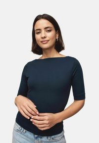 Navy blue fitted top made of smooth fabric, featuring short sleeves and a wide neckline. Paired with light denim jeans.