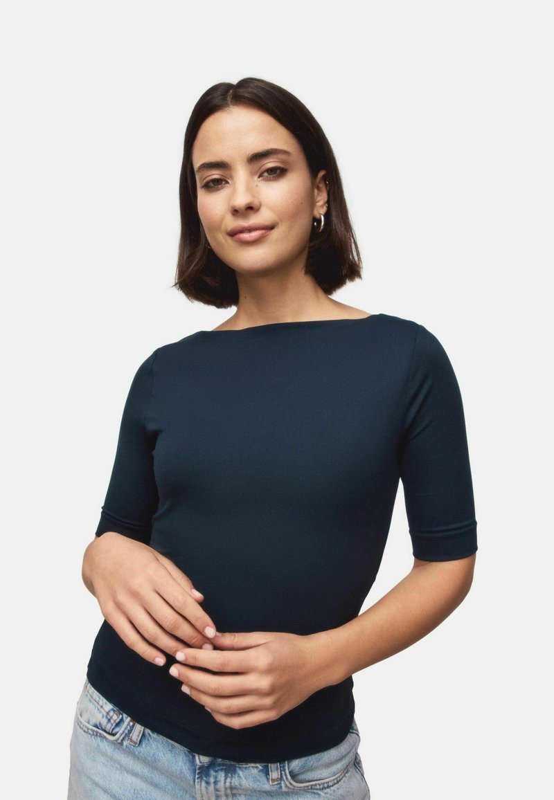 Navy blue fitted top made of smooth fabric, featuring short sleeves and a wide neckline. Paired with light denim jeans.