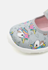 Grå slip-on sko med enhörning och blommönster, texturerat tyg och en vit gummisula. Inredningen har en mjuk rosa foder.